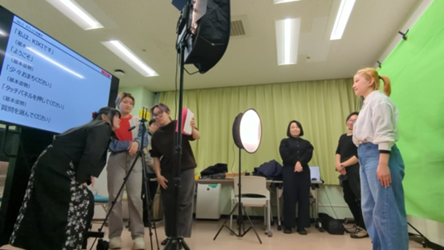 手話CG映像収録の様子。左側に大型モニターがあり、その向かい側で手話を表出している。