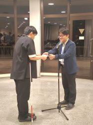 イブニングセッションでのショートビデオ受賞式にて、大会長の中澤先生(右)から賞状を受け取る川本さん(左)の写真